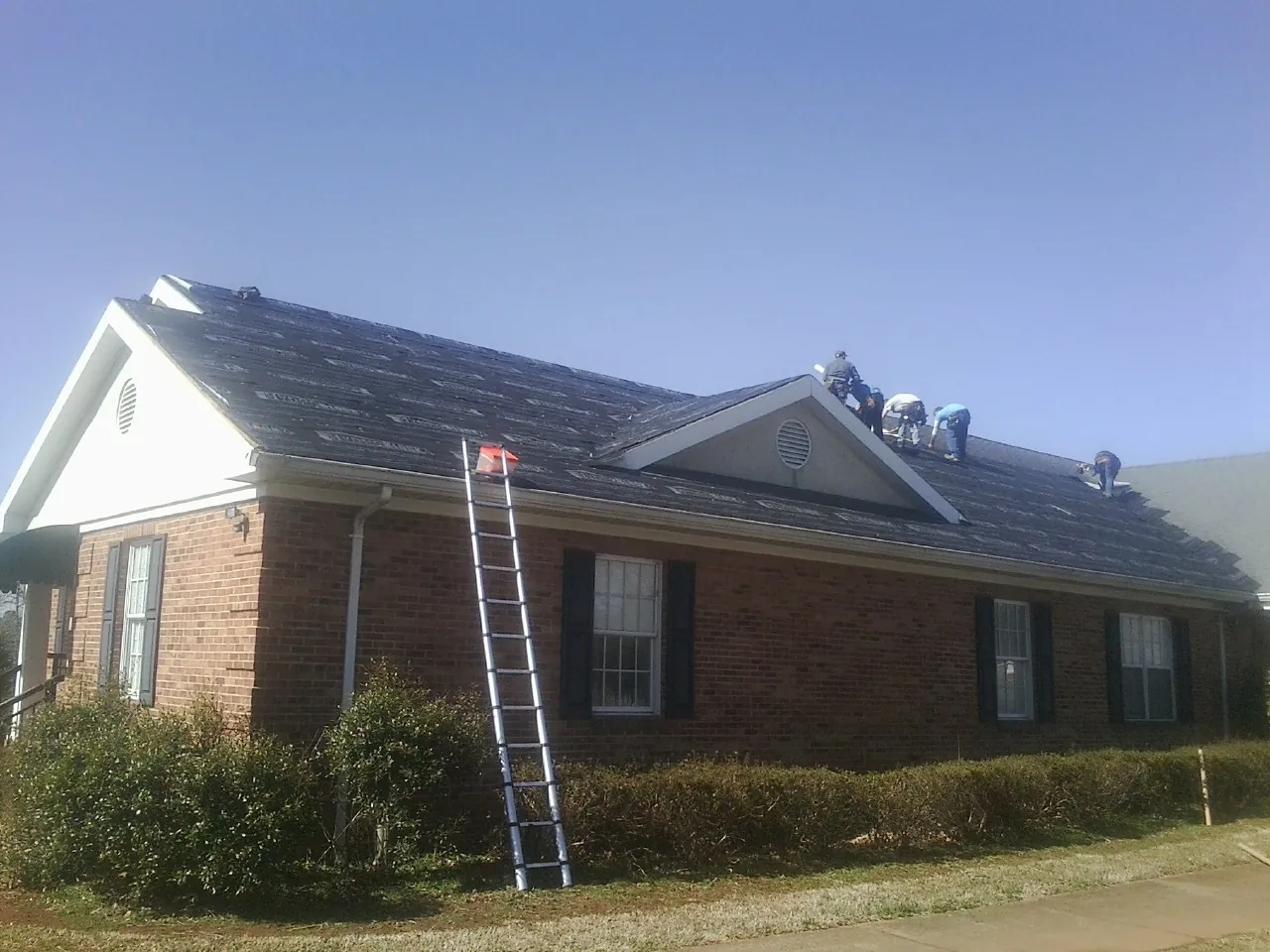 Crew tearing shingles off a brick ranch roof with a ladder set — Emergency Roof Repair work by our crew in South Pasadena