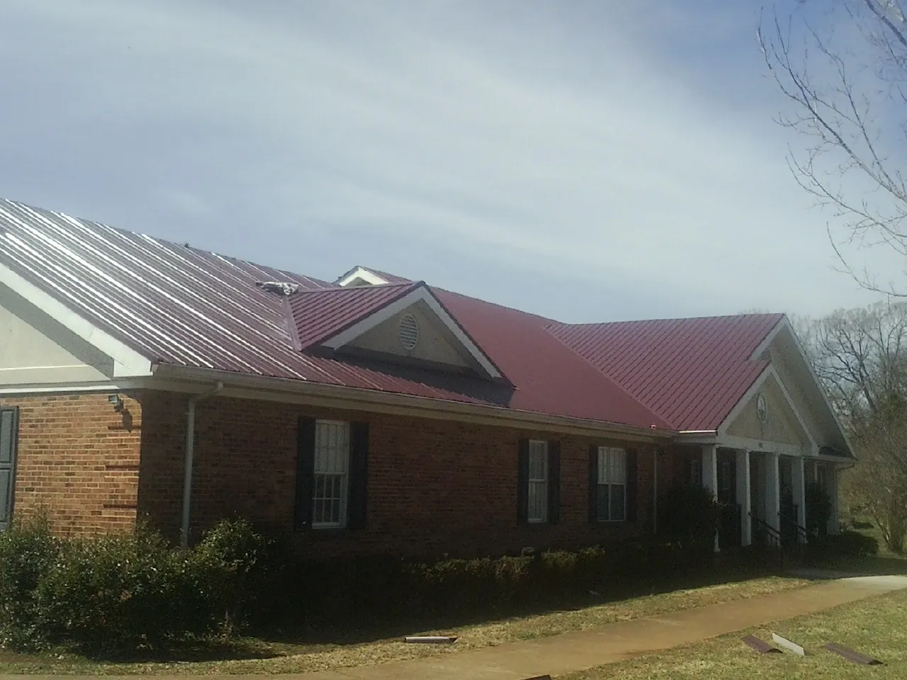 Red metal roof with gabled entries on a long brick building, from a Hail Damage Roof Repair job in South Pasadena