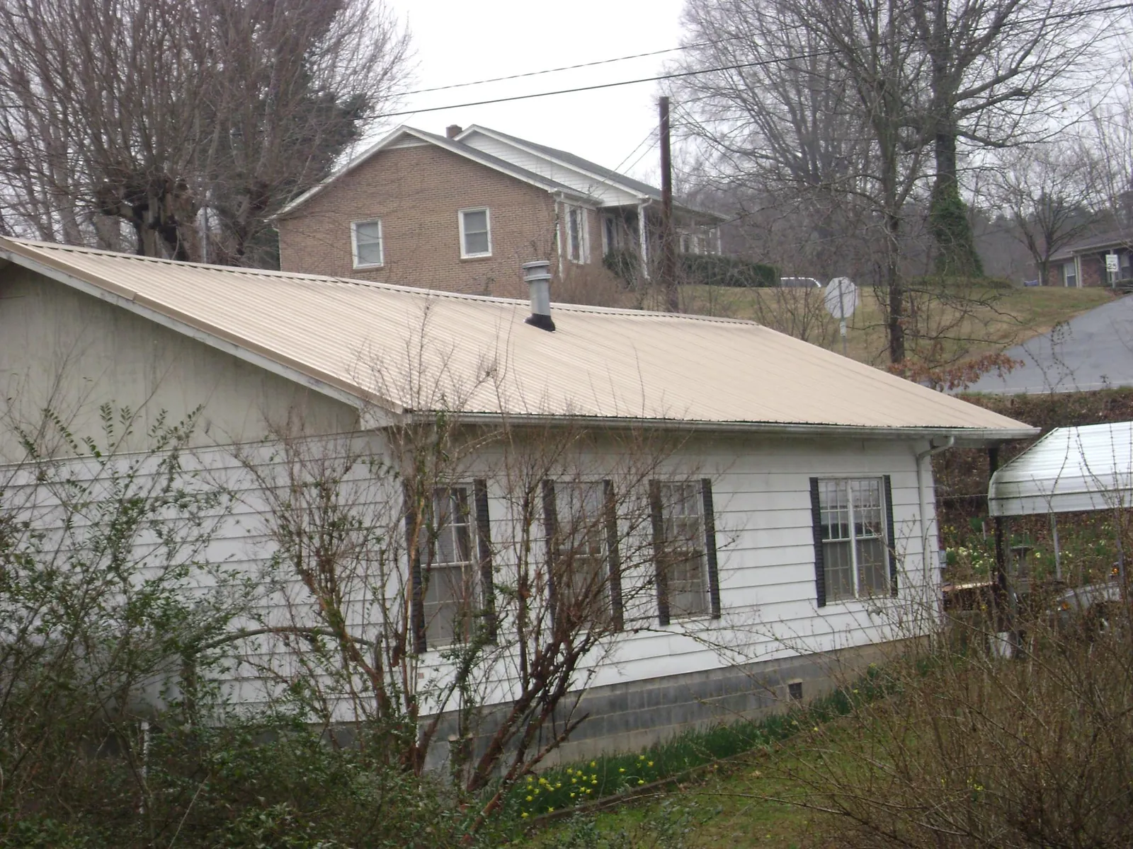 Tan metal roof on a white sided house set into a hillside — Commercial Roofing by Roofing Brothers in South Pasadena